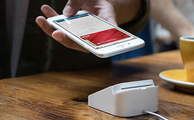 An iPhone touching to a payment terminal to pay with Apple Pay